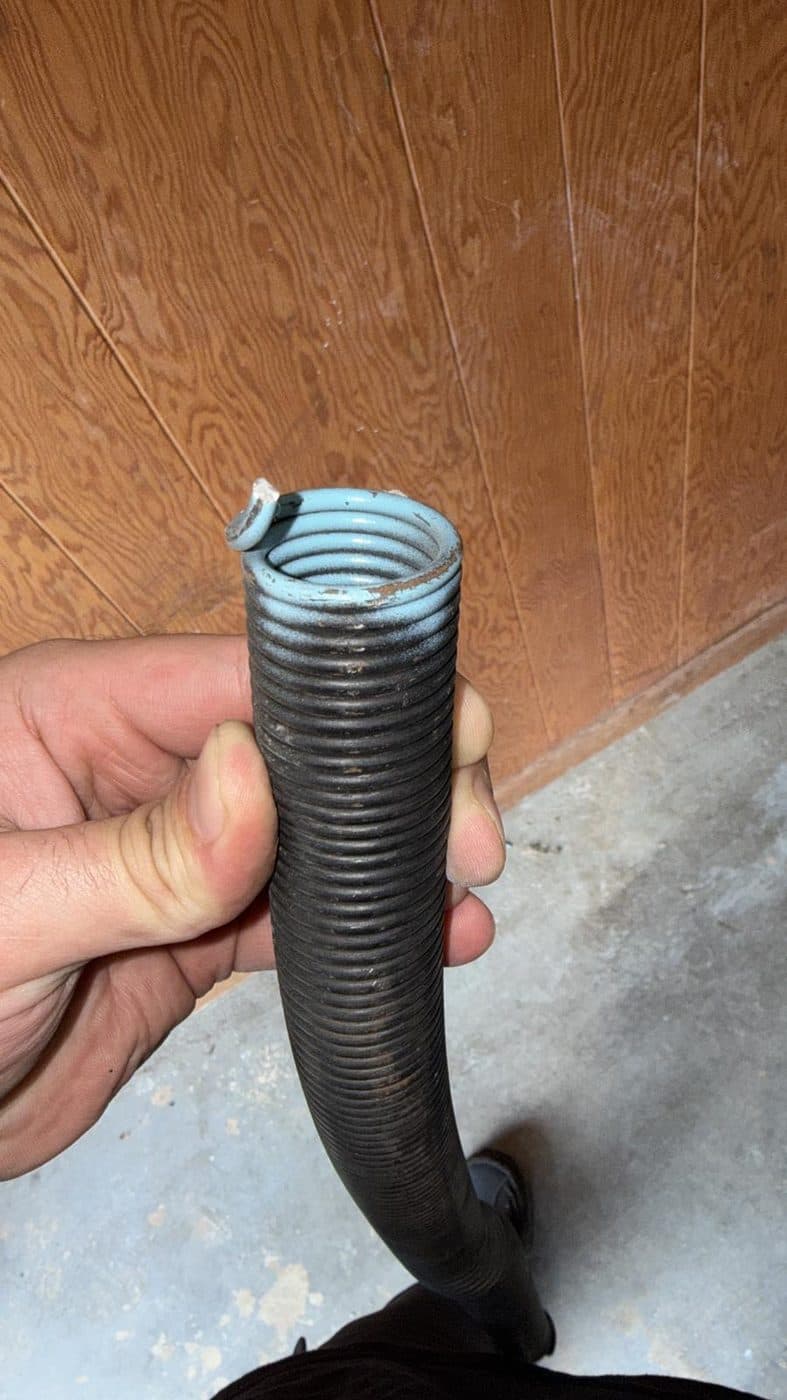 A snapped torsion spring held in the technician's hand, the coil pulled open where the steel failed.