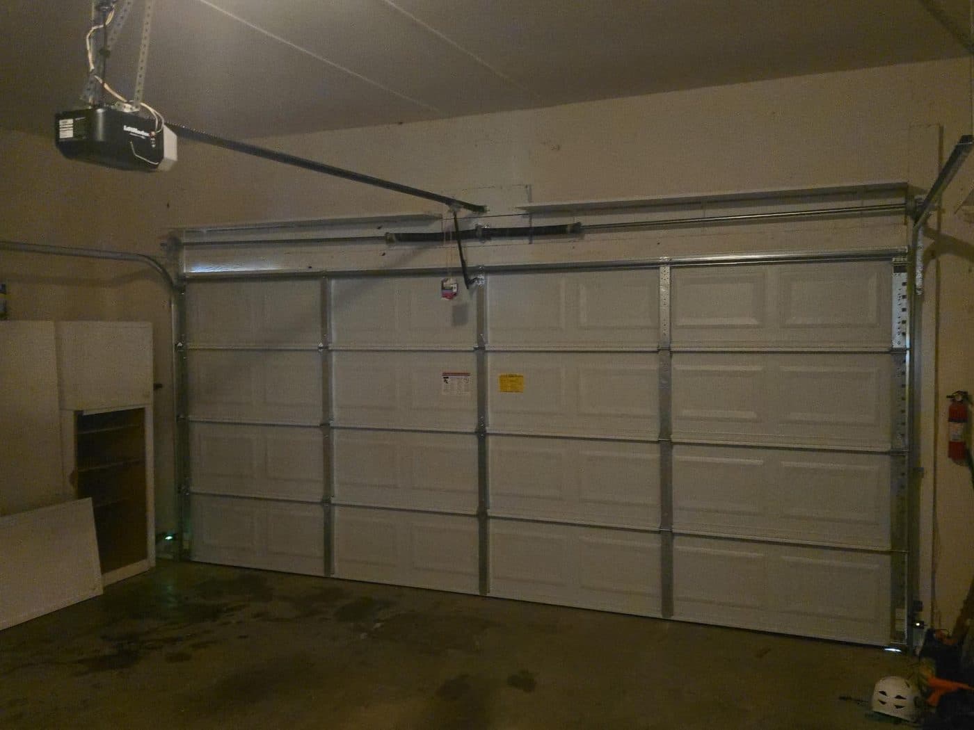 A fitted white sectional garage door photographed from inside, with the opener rail and motor running back from the header.