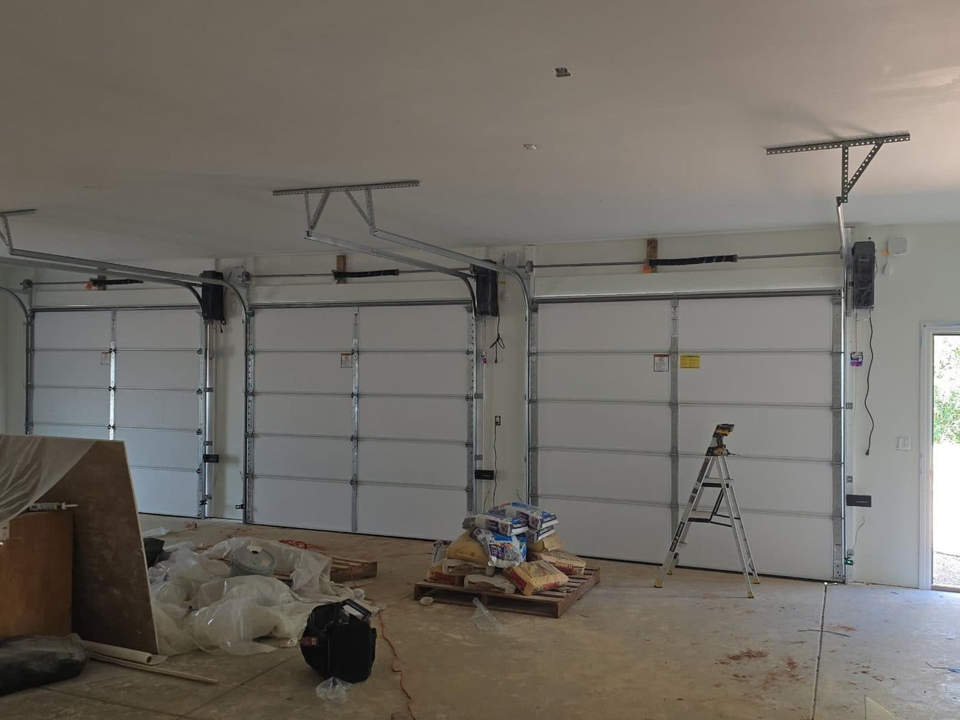 Two newly installed white sectional doors in an empty double garage, torsion shafts and tracks visible above.