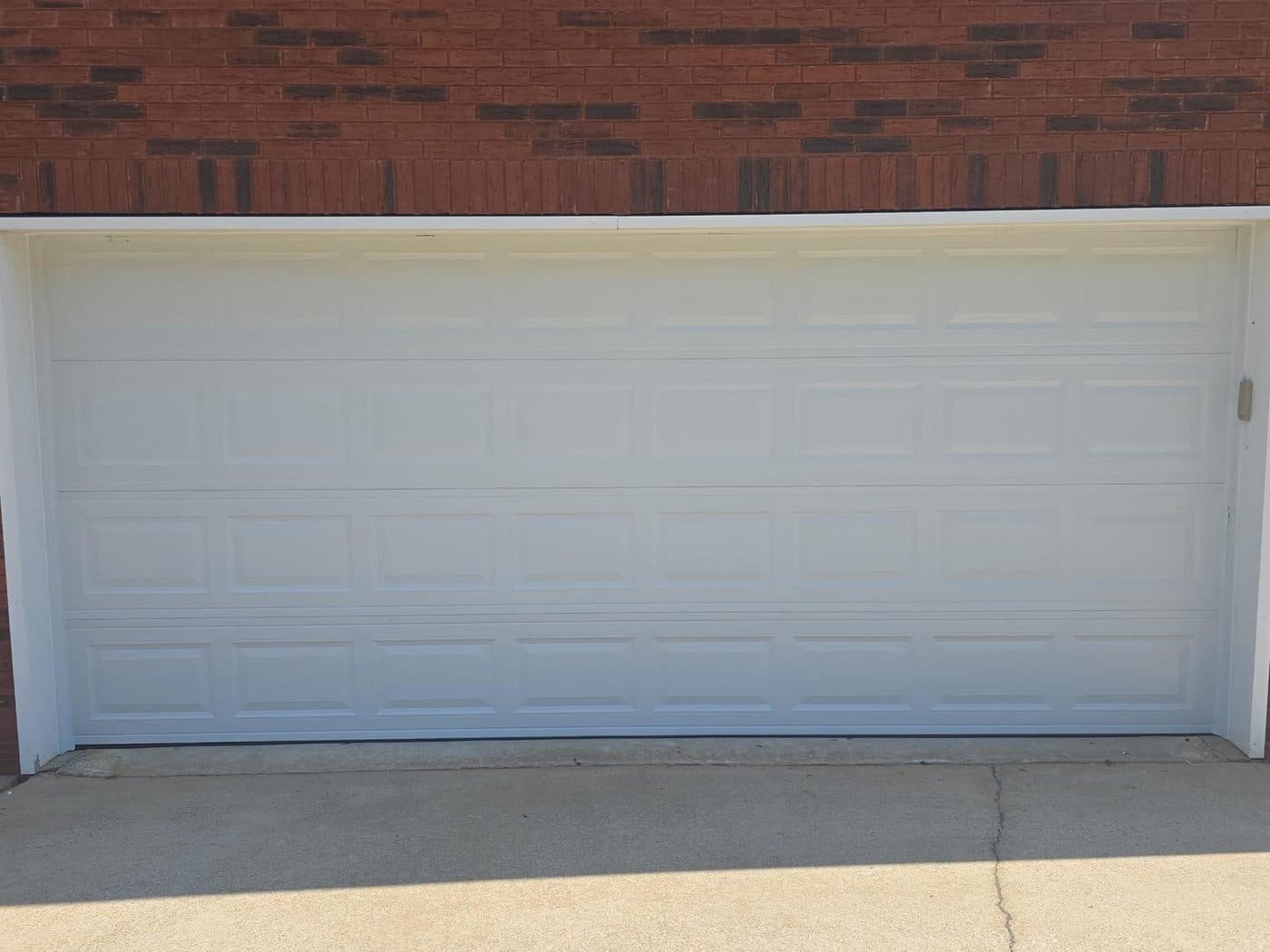 A finished white raised-panel double garage door on a red brick house, photographed from the driveway.