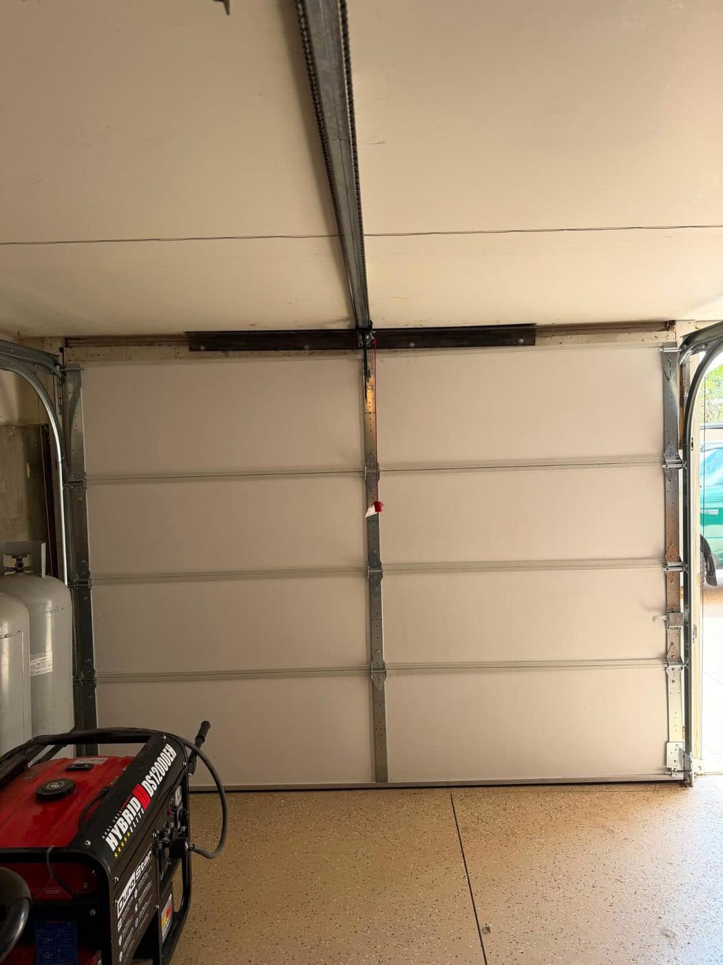A newly fitted torsion spring and shaft mounted above a closed cream sectional garage door, seen from inside.