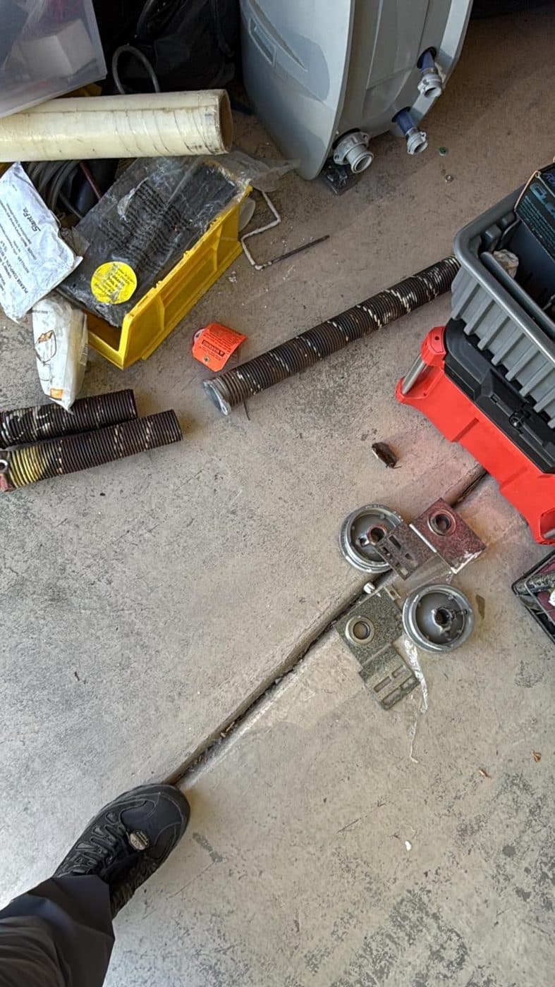 An extension spring and two pulleys laid out on a garage floor beside a toolbox after removal.